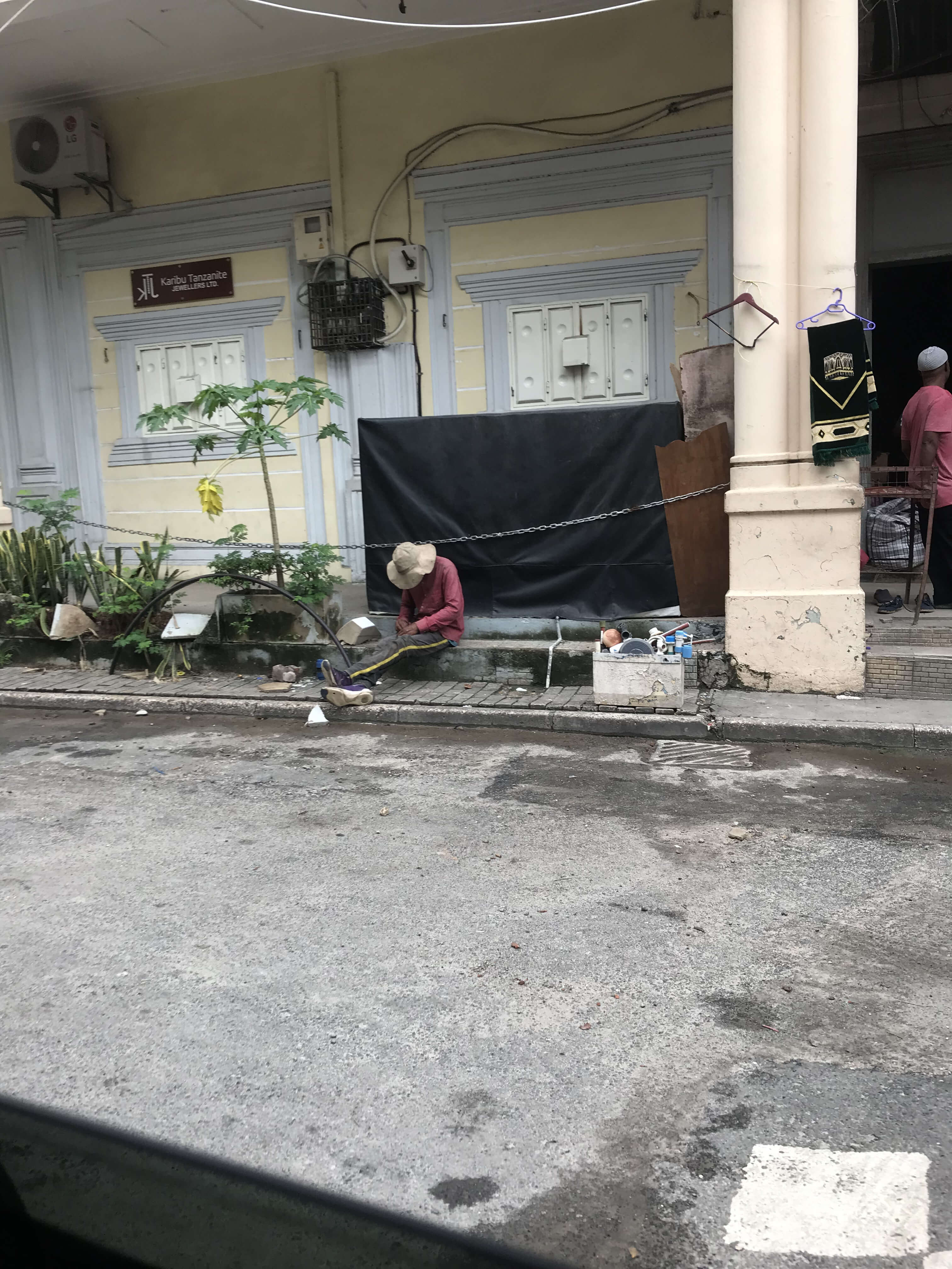 A man in a hat sleeping while sitting outside a store in Dar Es Salaam.